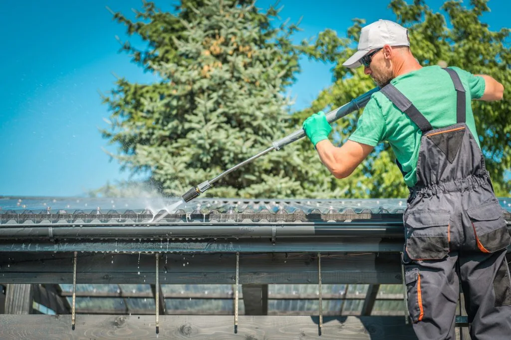 man washing the roof gutter of his house