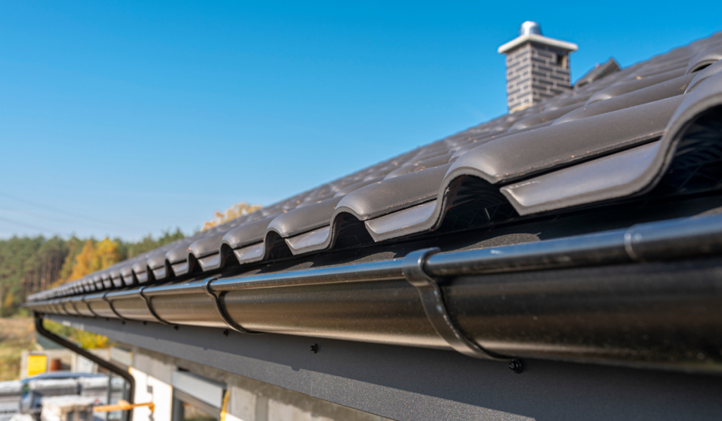 A metal, black gutter on a roof covered with ceramic tiles. Close up shot.