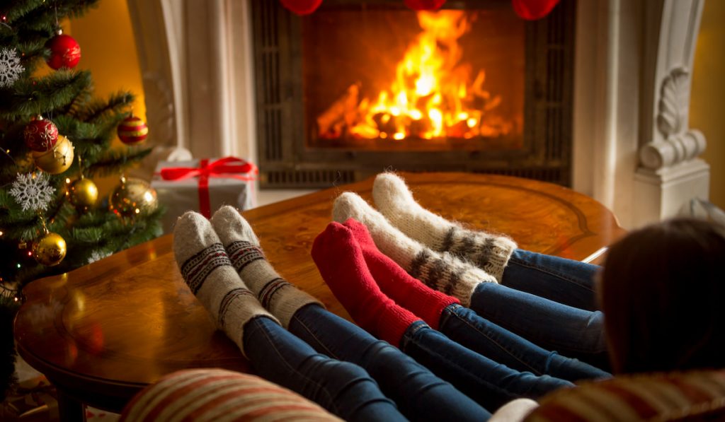 Feet of family in woolen socks warming at burning fireplace at living room 