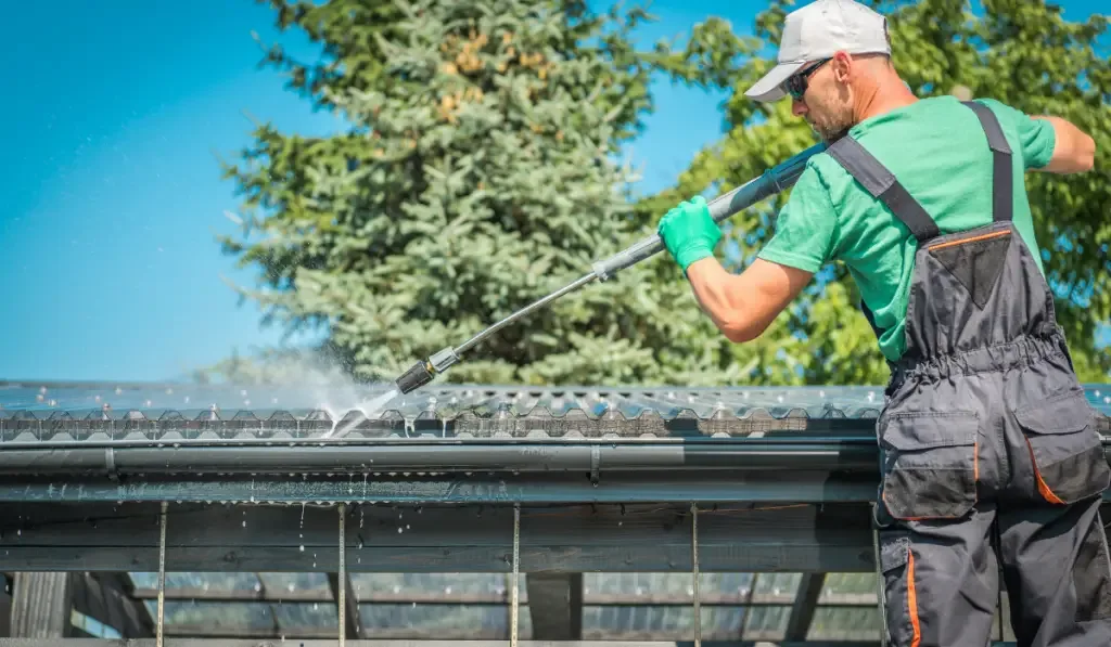 man cleaning the roof and gutter with hose and water
