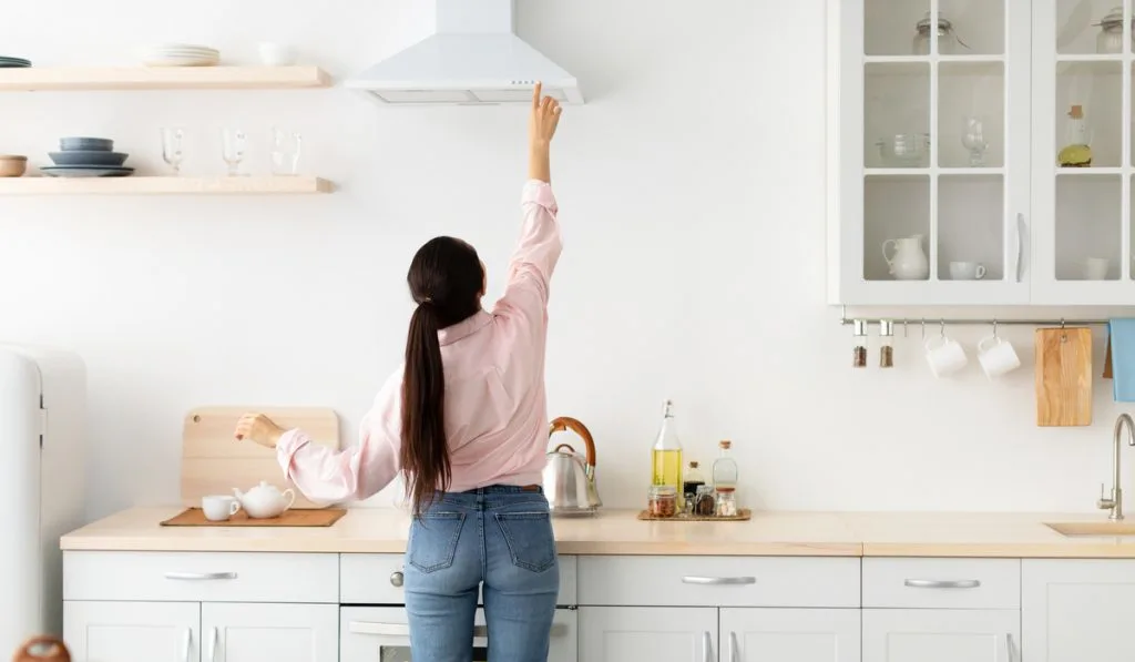 rear back view of young woman checking the exhaust fan in the kitchen 