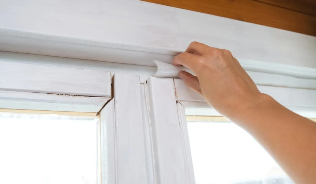 woman hand insulating old windows to keep house warm 