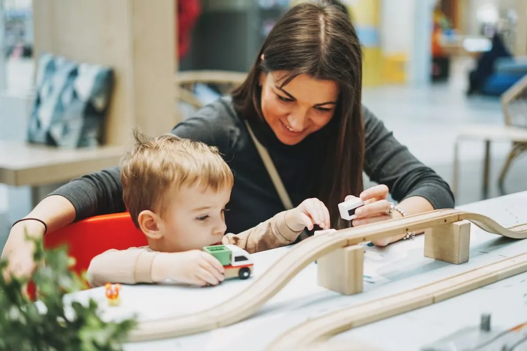 Cute baby boy toddler child with baby sitter play with car toys in game room