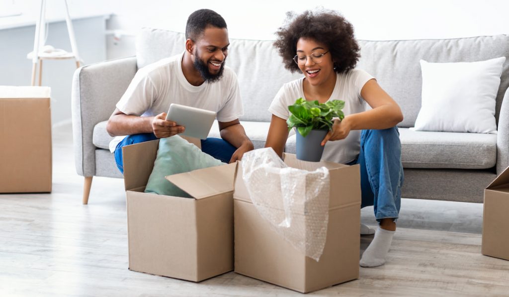 Young Couple Moving House Packing Belongings In Boxes Indoors
