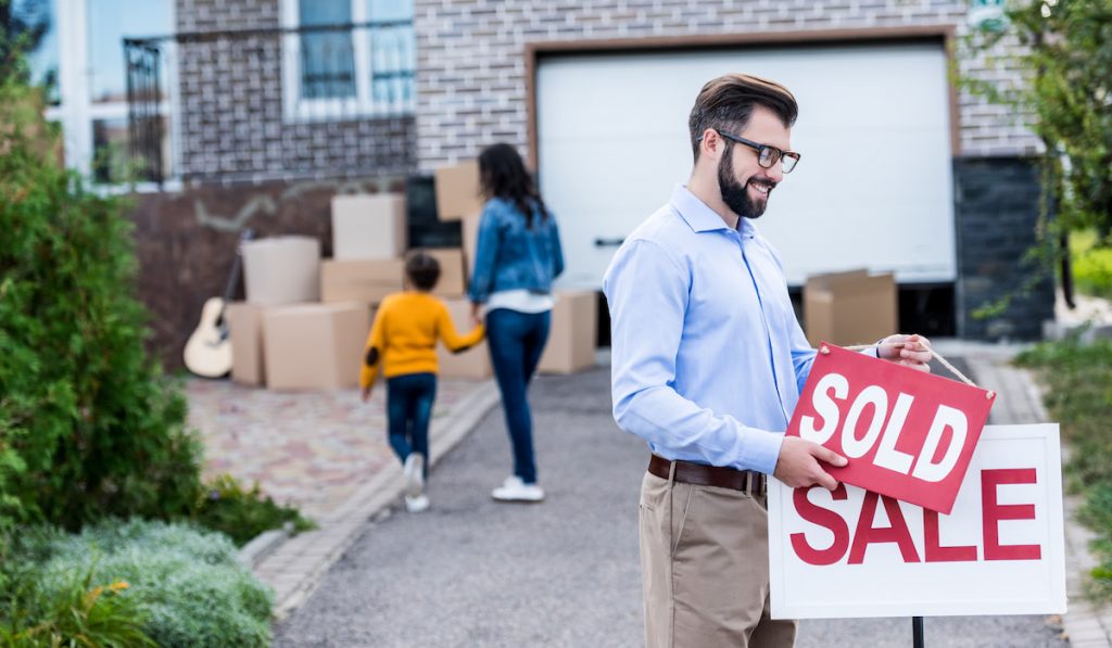 realtor hanging sold sign in front of people moving into new house

