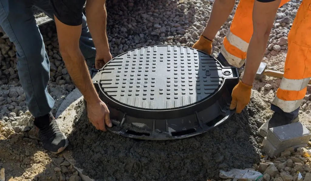 worker installs a sewer manhole on a septic tank made of concrete rings