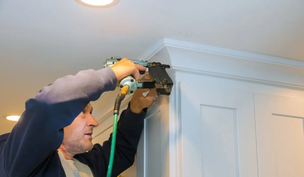 Air nailer tool close up of carpenter using nail gun to crown moldings on kitchen cabinets