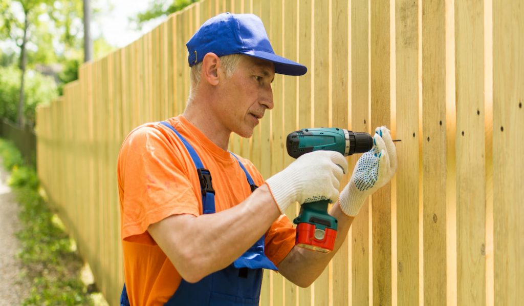 Carpenter installing new wooden fence holding electric drill