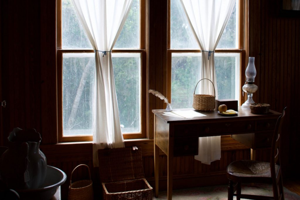 Filtered sunlight though farmhouse style windows highlighting objects in dim sitting room in old farmhouse