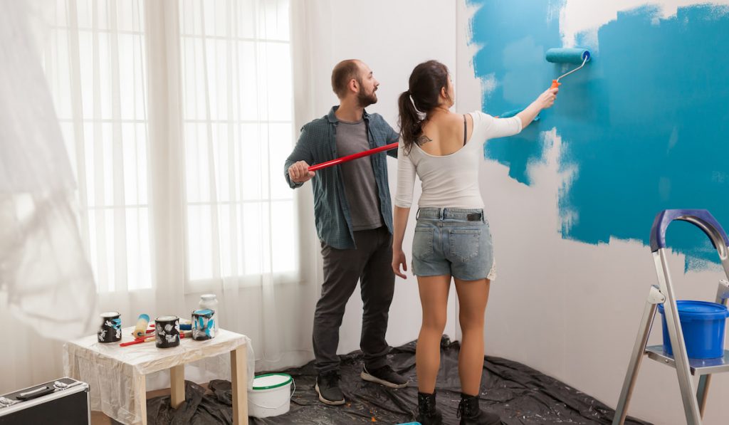 Home during renovation, couple painting their wall using roller paint brush with light blue paint color