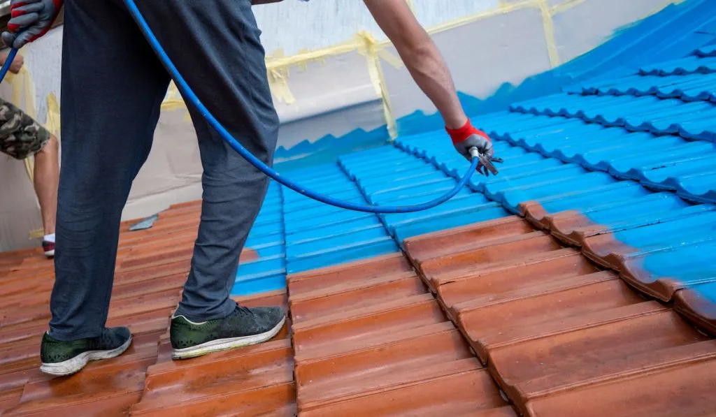 Professional worker painting roof tiles using spray paint high pressure equipment 