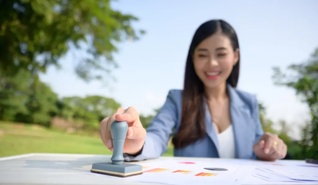 Close-up Of Businesswoman Hand Stamping Approved On Contract Paper
