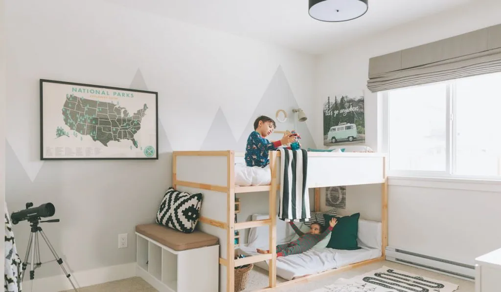 Two little boys playing on a bunk bed in a bright white children's bed room.
