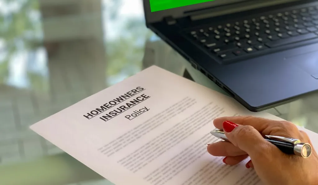 Woman in workspace with laptop & Homeowners Insurance Policy document being reviewed
