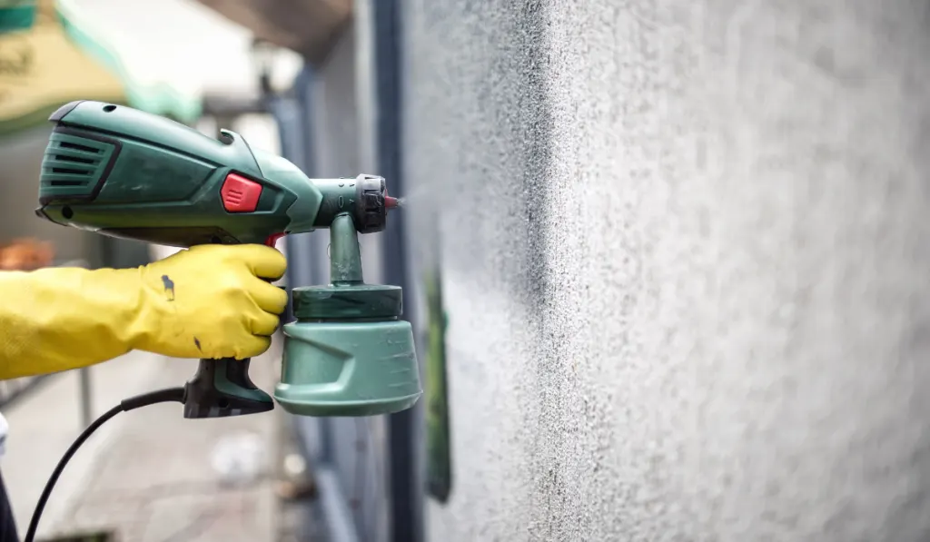 Worker painting wall with grey paint using a professional spray gun. 