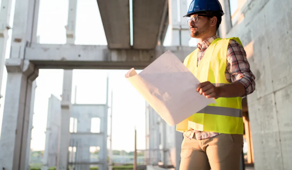 Portrait of male site contractor engineer with hard hat holding blue print paper
