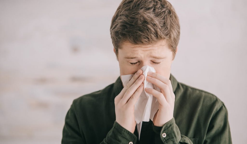 man having allergy and sneezing in tissue at home