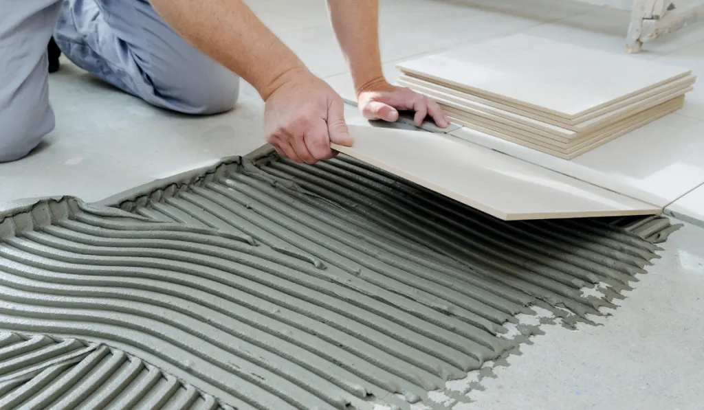 The hands of the tiler are laying the ceramic tile on the floor.