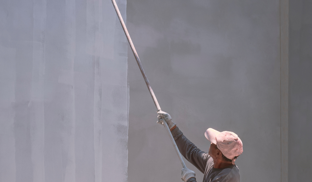 Construction worker painting white primer color on cement wall inside of house construction site
