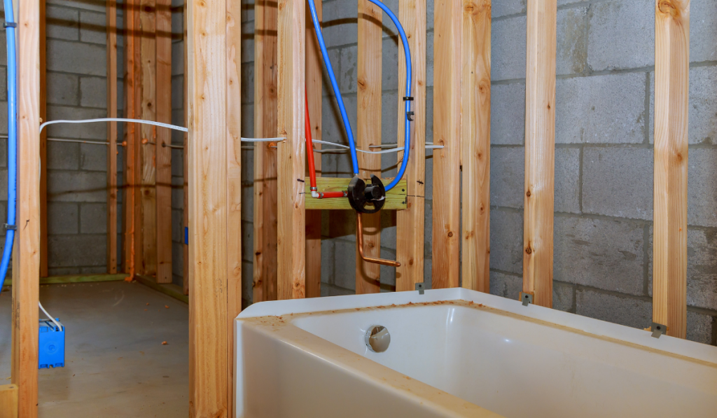 Bathroom remodel showing under floor plumbing work connecting old copper pipes to new plastic ones 