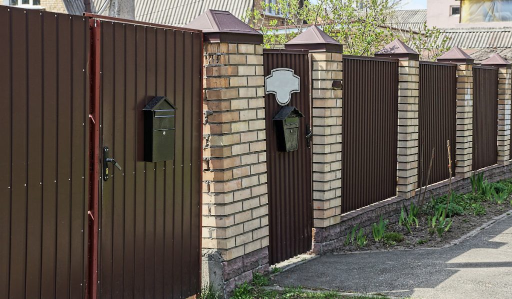 Brown metal gate and door with black mailboxes attached to it near a rural street