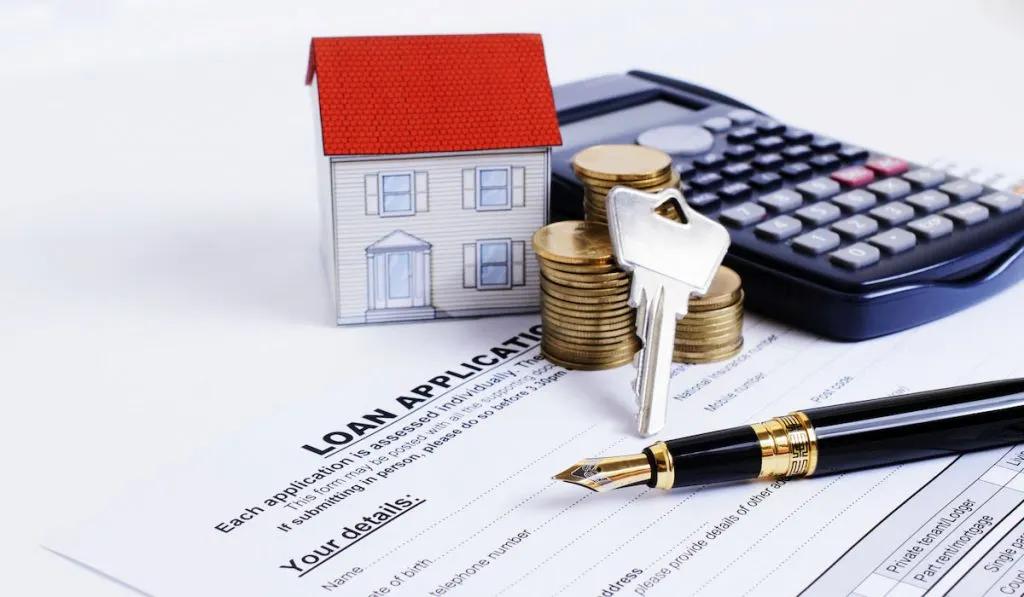 Fountain pen and key and calculator and paper house and coins stack on Loan Application form for House loans 