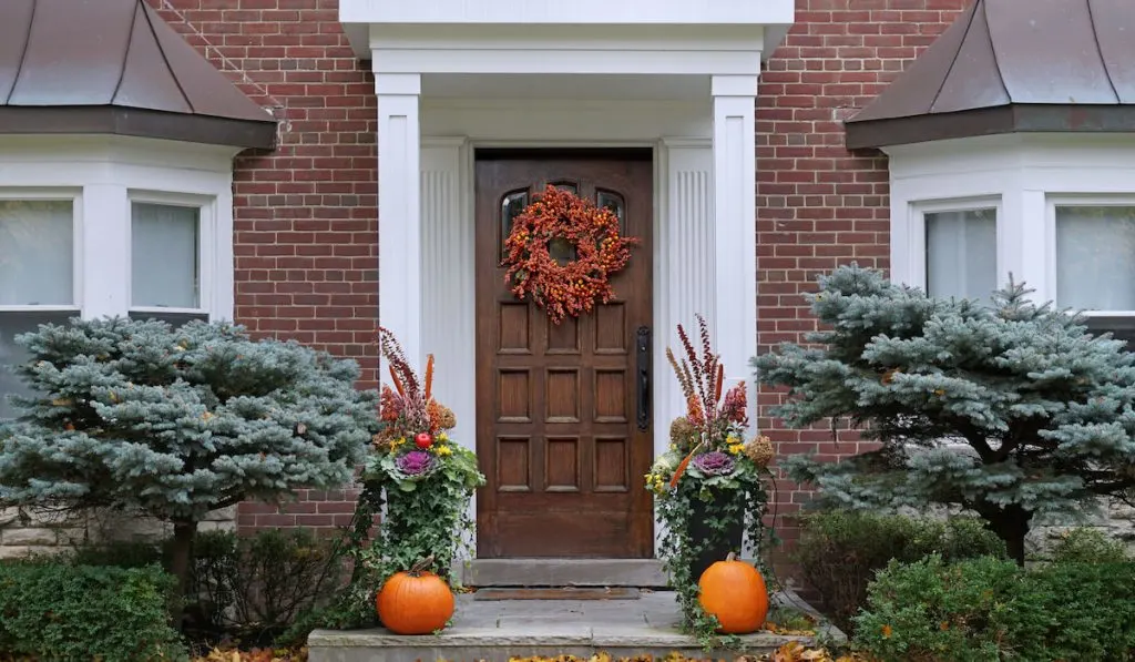 Front door with bushes, colorful fall wreath and pumpkins
