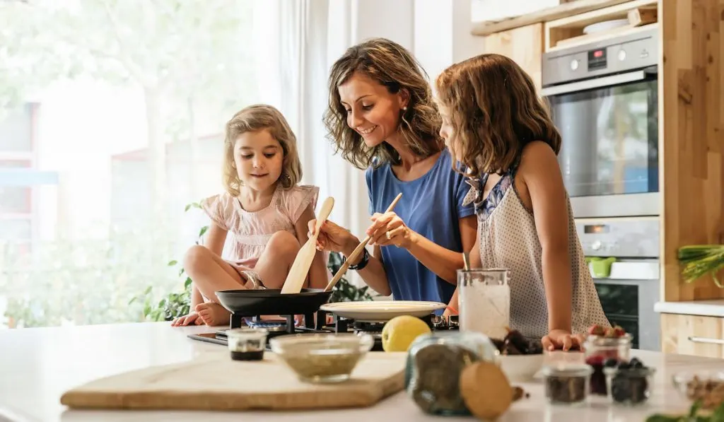 Little sisters cooking with her mother in the kitchen.