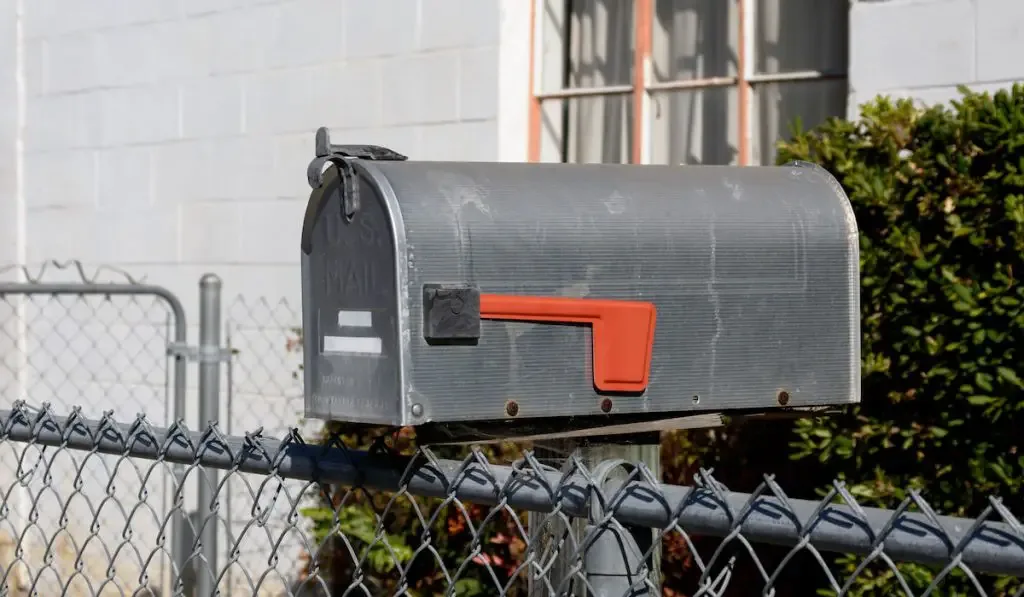 Mailbox with lowered red flag inside wire fence of a house