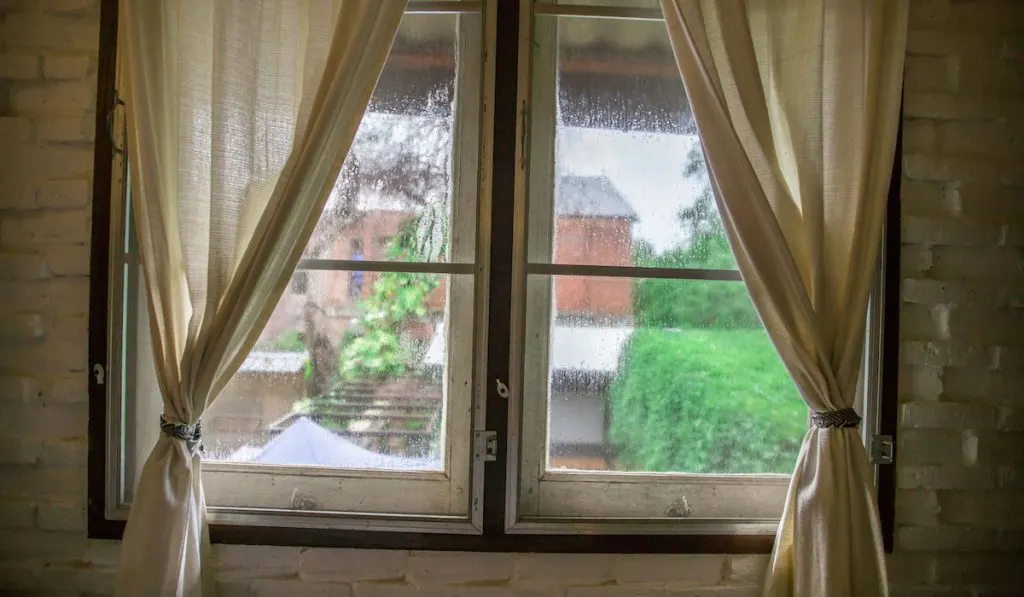 Old window with curtains inside the room showing blurred background outside