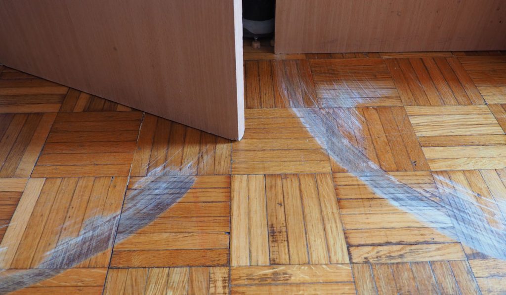 Scratched parquet flooring in the room. Scratches, chips and dents on the floor.