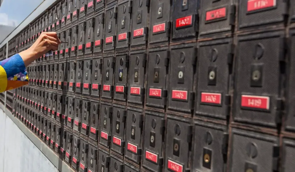 Woman hand holding a key and unlocking a PO box, in the long row of PO boxes
