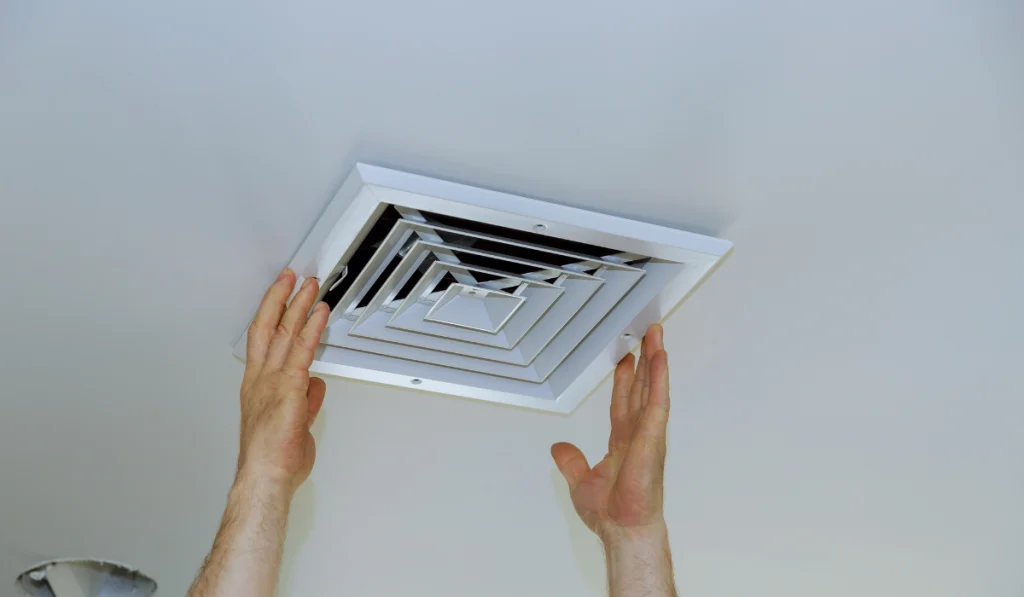 Close up man hand installing vent cover from ceiling Mounted Air Conditioner.
