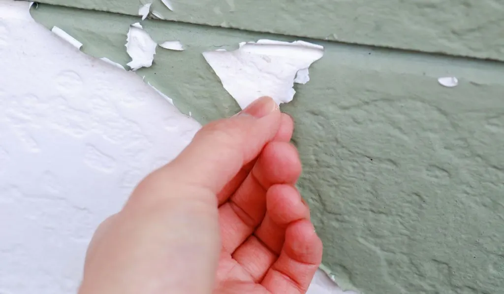 A hand holding a peeling paint from a wall of a house