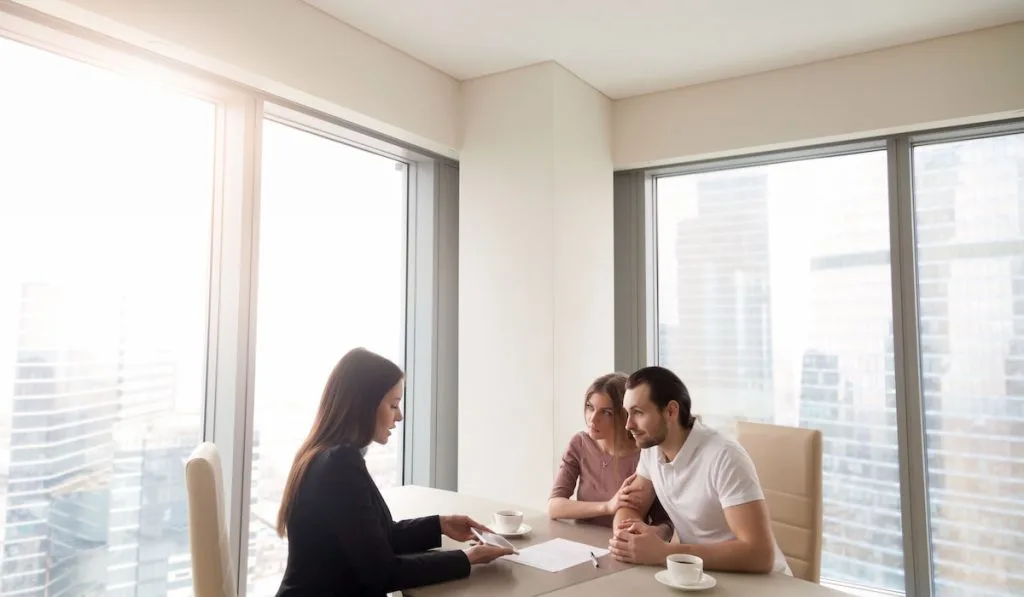 Bank representative discussing requirements and calculation for housing loan contract with the couple in the office