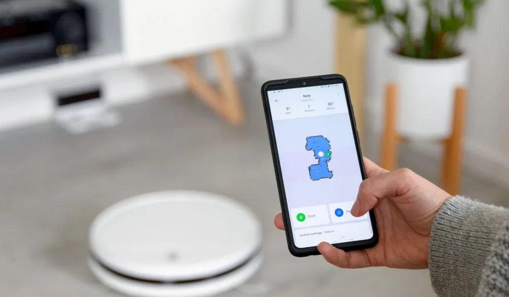 Hand holding mobile phone and using app assigning maps controlling roomba vacuum cleaner