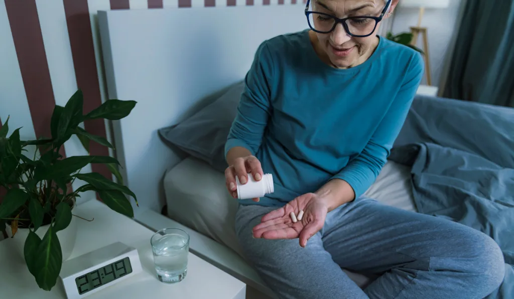 Melatonin for promotion of healthy sleep. Mature woman taking melatonin supplement pill before bed