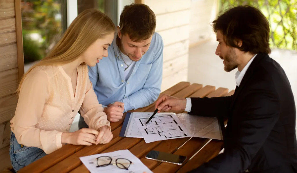 Property manager showing house plan to his clients at table on porch
