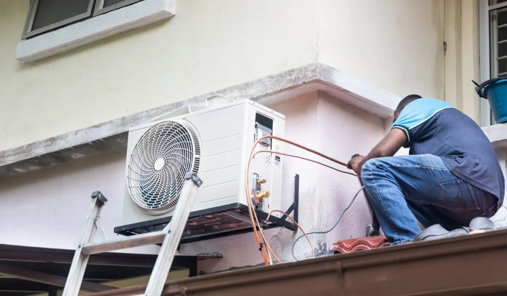 Technician installing outdoor air conditioner compressor unit on wall