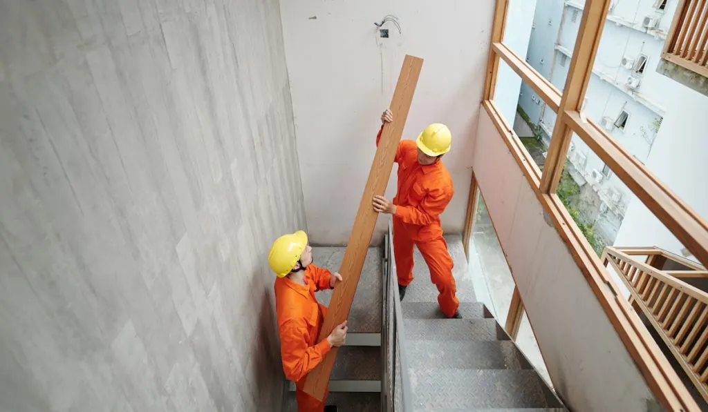 Workers carrying a long woodboard up the narrow stairs of a new house under construction