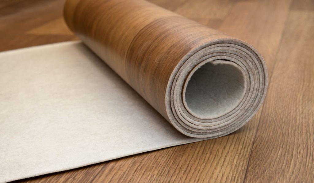 An expanded roll of brown linoleum lies on the floor