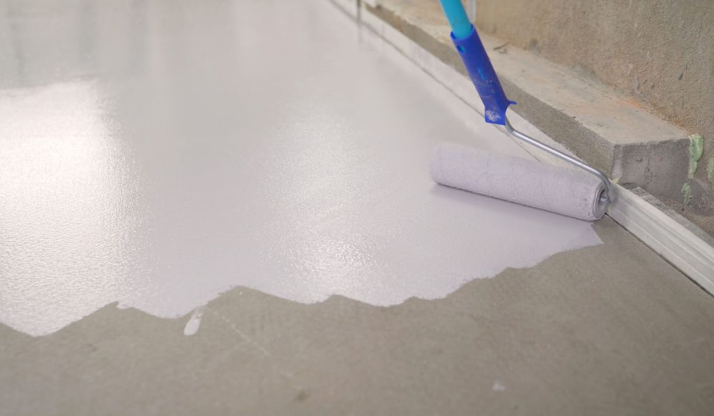Worker paints the concrete floor with white paint using a roller