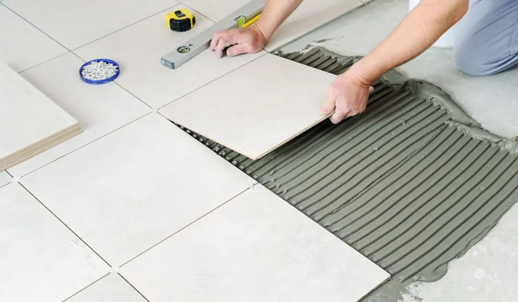 hands of the worker are laying the ceramic tile on the floor